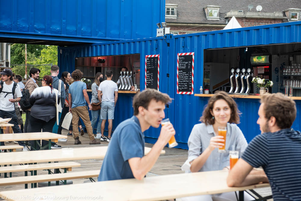 Des personnes boivent une bière en terrasse devant des containers bleus à Phare Citadelle