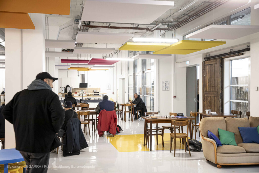 Intérieur de la T'rêve à la Cave à Vins - La Salle Commune - Des personnes assises sur des chaises et une kitchenette en fond de salle