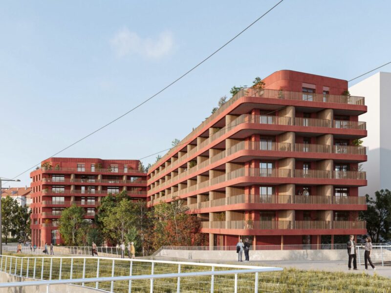 Un bâtiment de 6 étages, rouge avec des loggias bordées de balcons filants incurvés aux angles.