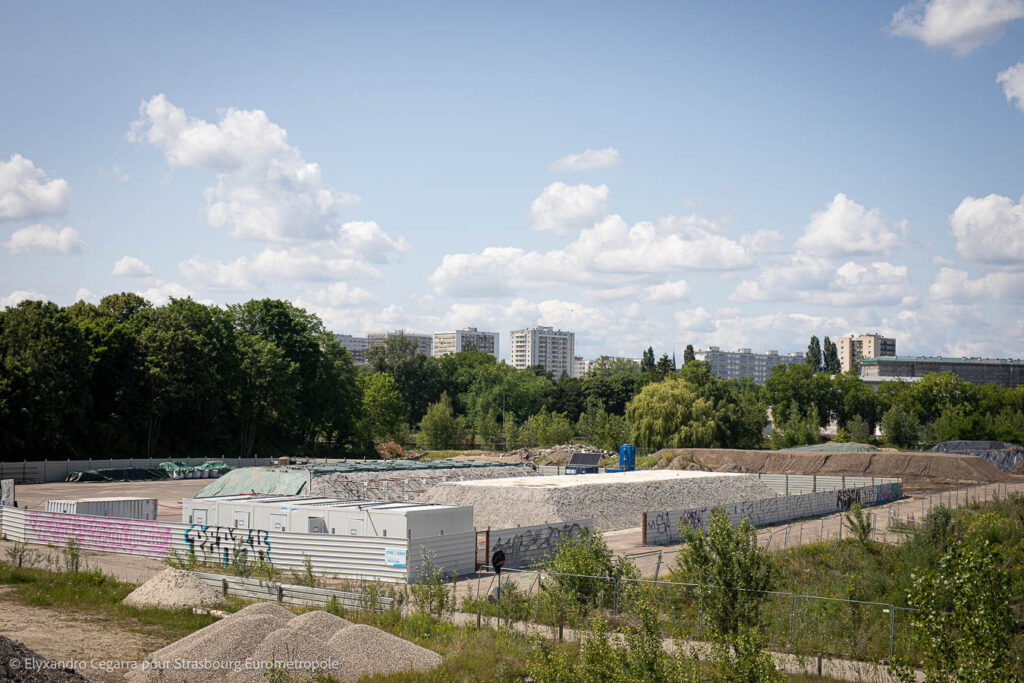 Vue sur la plateforme de désorption thermique installée au nord de la presqu'île Citadelle : on voit des tas de terre couverts de béton et un bâtiment modulaire au sein d'une enceinte clôturée.