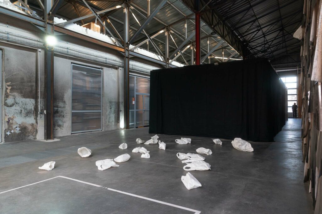 Des sacs plastiques blancs en céramique jonchent un sol en béton ciré : Une installation de Petra Keinhorst dans le cadre de la Regionale 26 à Garage Coop © Alex Flores