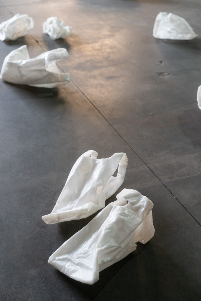 Des sacs plastiques blancs en céramique jonchent un sol en béton ciré : Une installation de Petra Keinhorst dans le cadre de la Regionale 26 à Garage Coop © Alex Flores