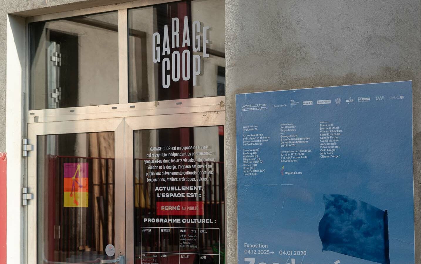 La porte de l'exposition Zoodyssée de la Regionale 26 à Garage Coop : on voit une porte vitrée et une affiche représentant un drapeau devant l'océan