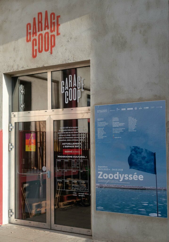 La porte de l'exposition Zoodyssée de la Regionale 26 à Garage Coop : on voit une porte vitrée et une affiche représentant un drapeau devant l'océan