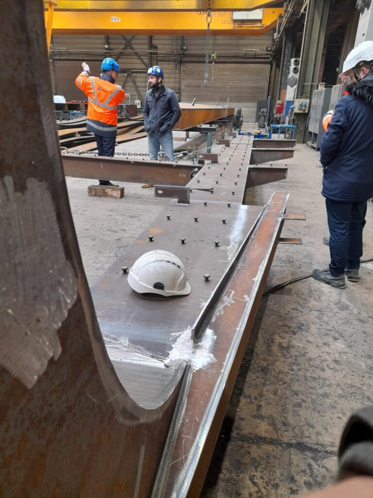 Des personnes casquées inspectent une structure rivetée de la passerelle