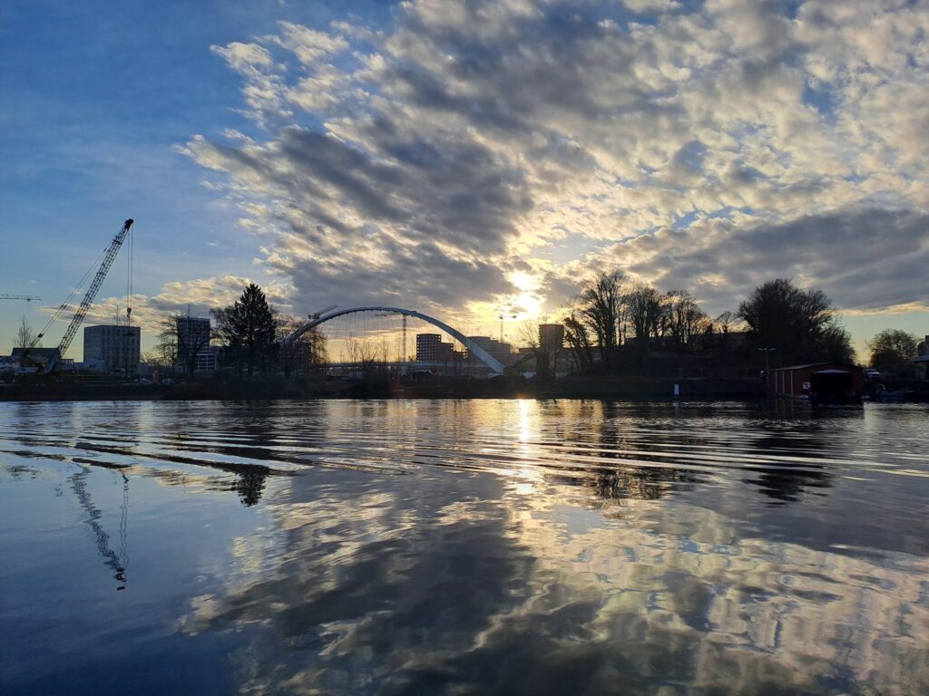 Vue sur le bassin dusuzeau au raz de l'eau avec la grue qui domine la plate forme de montage du chantier de l'autre côté de l'eau. On voit également les grues et bâtiments du quartier Starlette et l'arche du pont andré bord en arrière plan