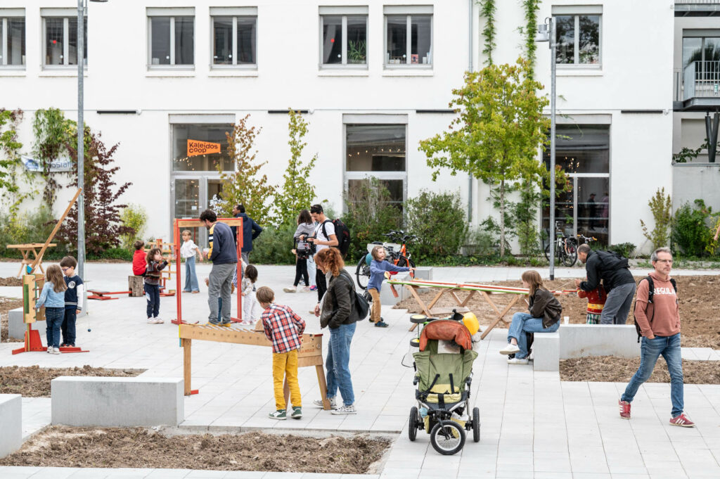 Des enfants et leurs parents jouent sur une place avec des jeux en bois.