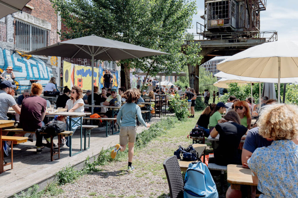 Un enfant court entre deux rangées de tables et de parasols sur la terrasse verdoyante de Phare Citadelle.