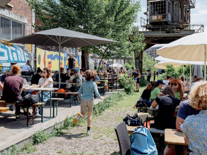 Un enfant court entre deux rangées de tables et de parasols sur la terrasse verdoyante de Phare Citadelle.