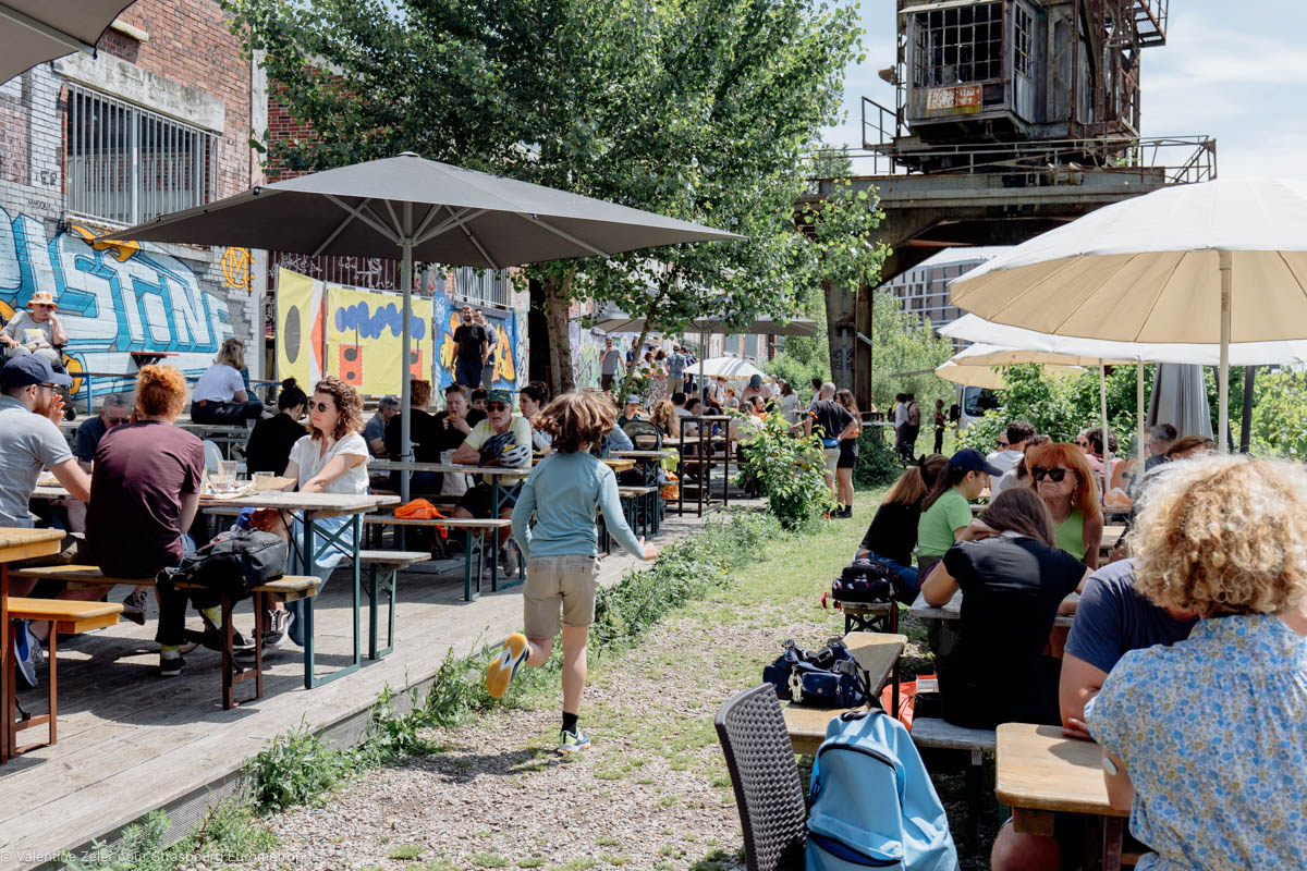 Un enfant court entre deux rangées de tables et de parasols sur la terrasse verdoyante de Phare Citadelle.
